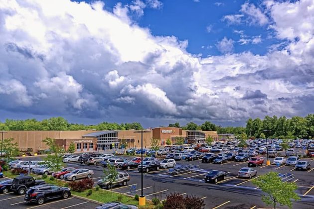 Large Walmart store with a full parking lot under a sky filled with thick, white and gray clouds.